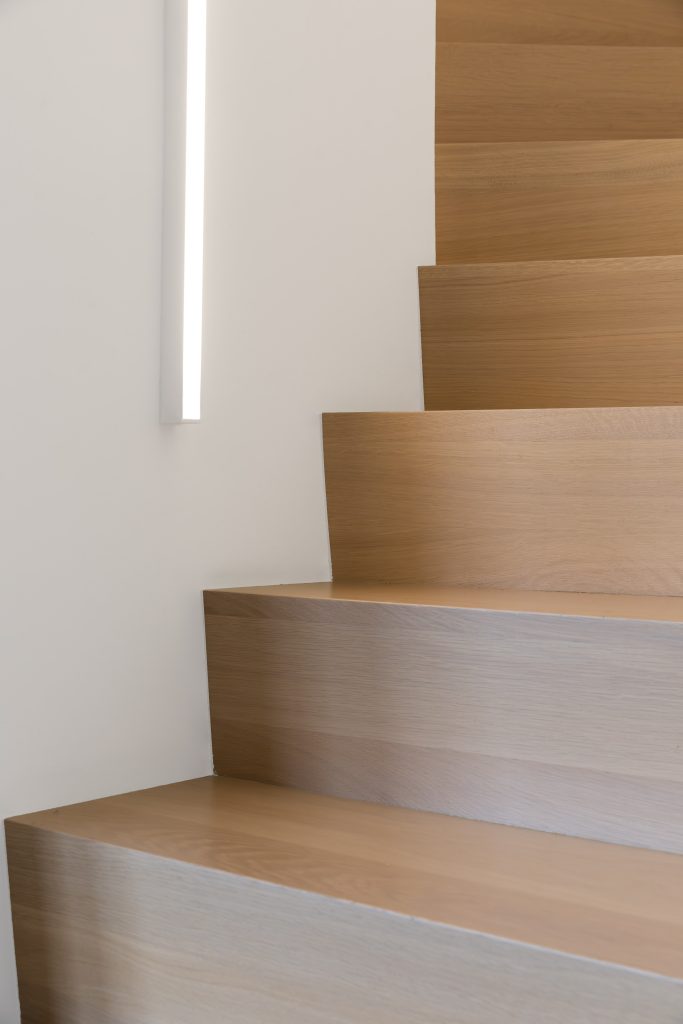 Escalier en béton recouvert de marches et contre-marches en chêne 3 plis. e garde-corps à l'étage est en MDF laqué et satiné blanc